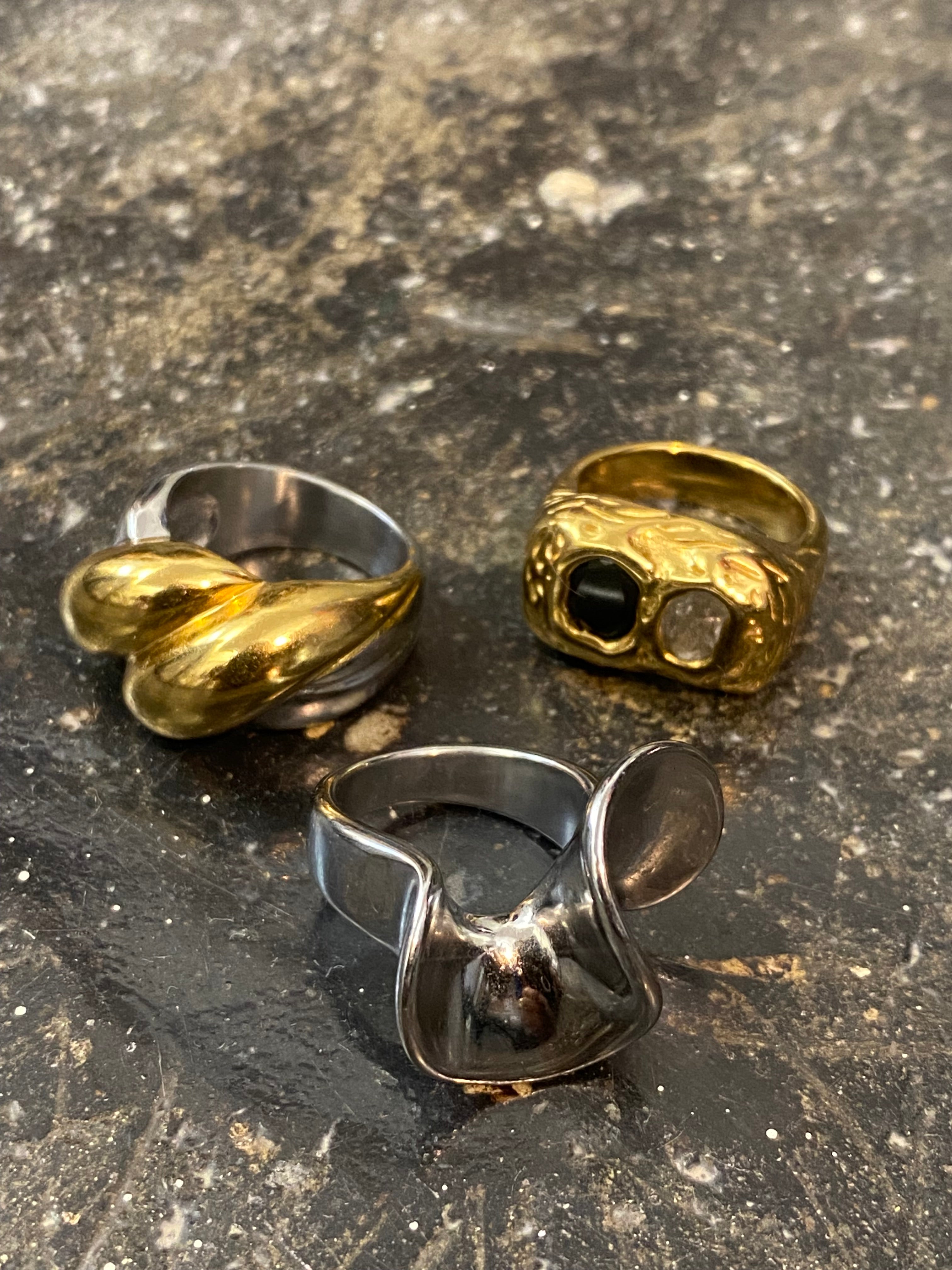 Mixed metal statement rings including the GRISÉ NYC 2-Tone Rugged Ring displayed on a textured stone surface.