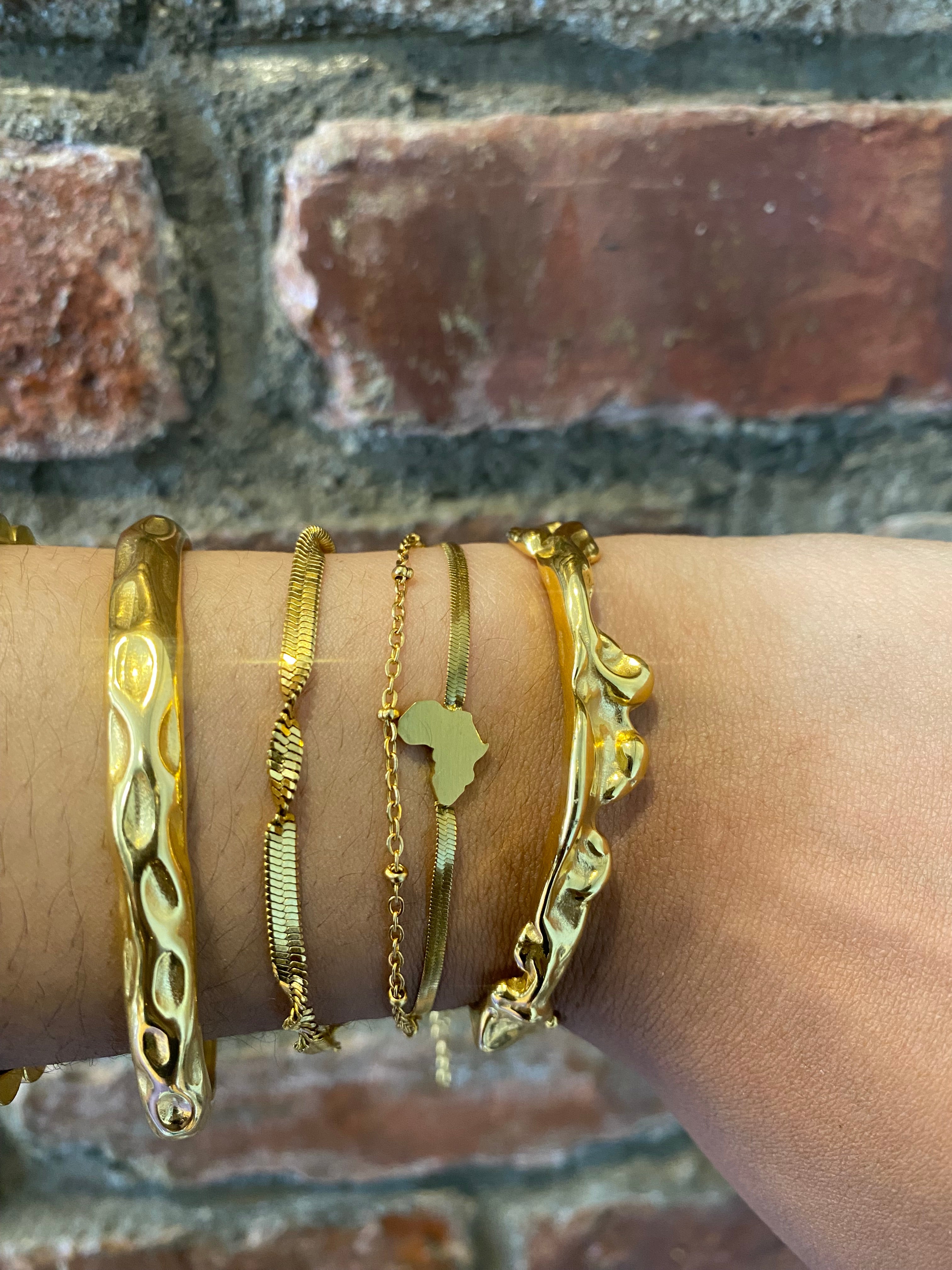 Model wearing twisted flat snake chain gold bracelet and other statement bracelets by GRISÉ NYC.