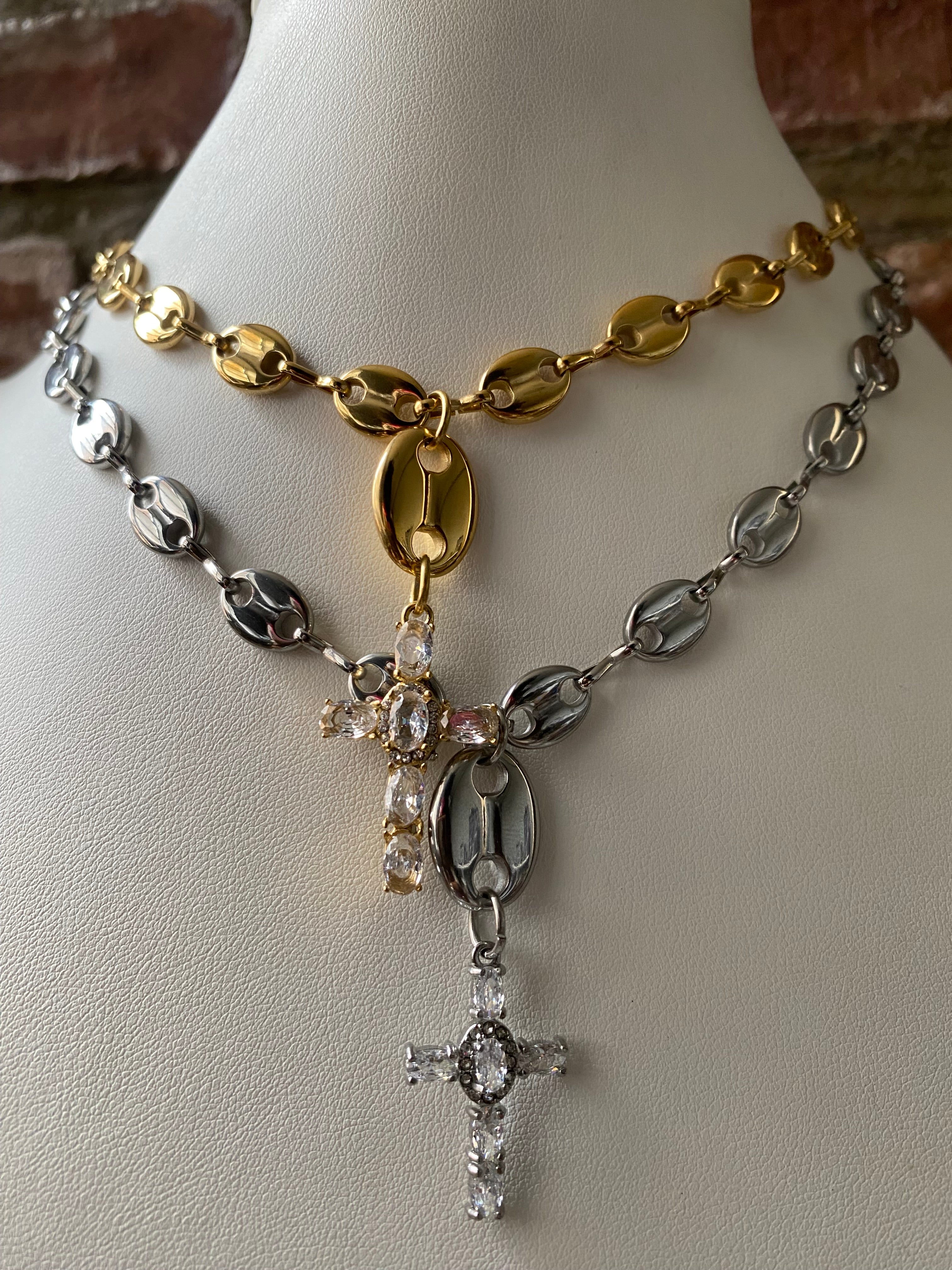 Layered mariner link cross pendant necklaces in gold and silver stainless steel worn together close up.