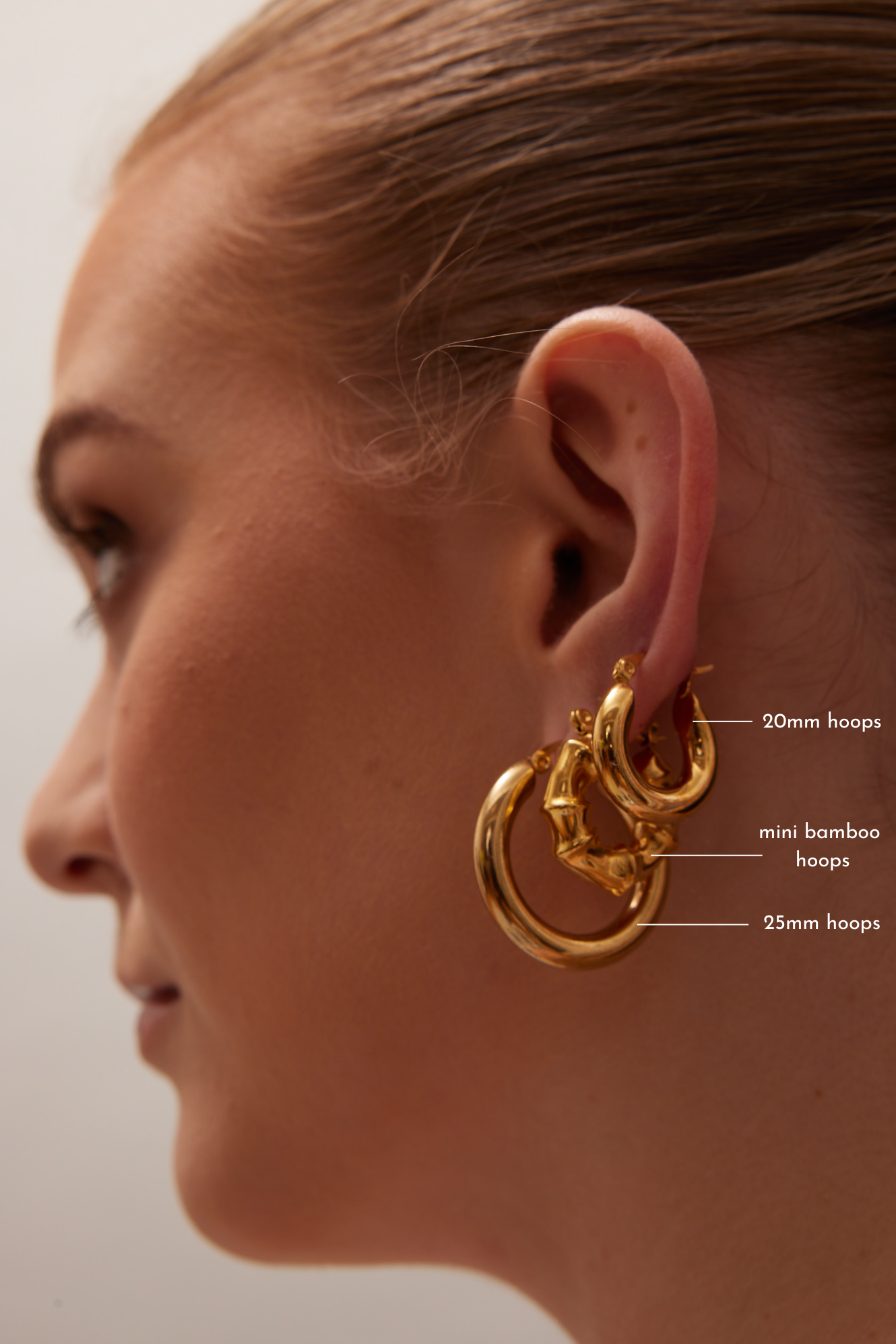 Model wearing stacked 20 mm 18K gold mini hoop earrings in a layered ear styling by GRISÉ NYC.