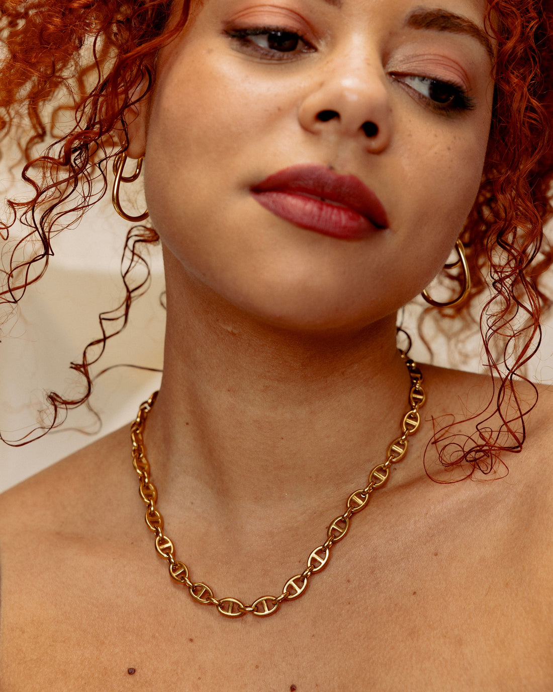 Close-up of a person wearing a gold mariner link chain necklace with a neutral background