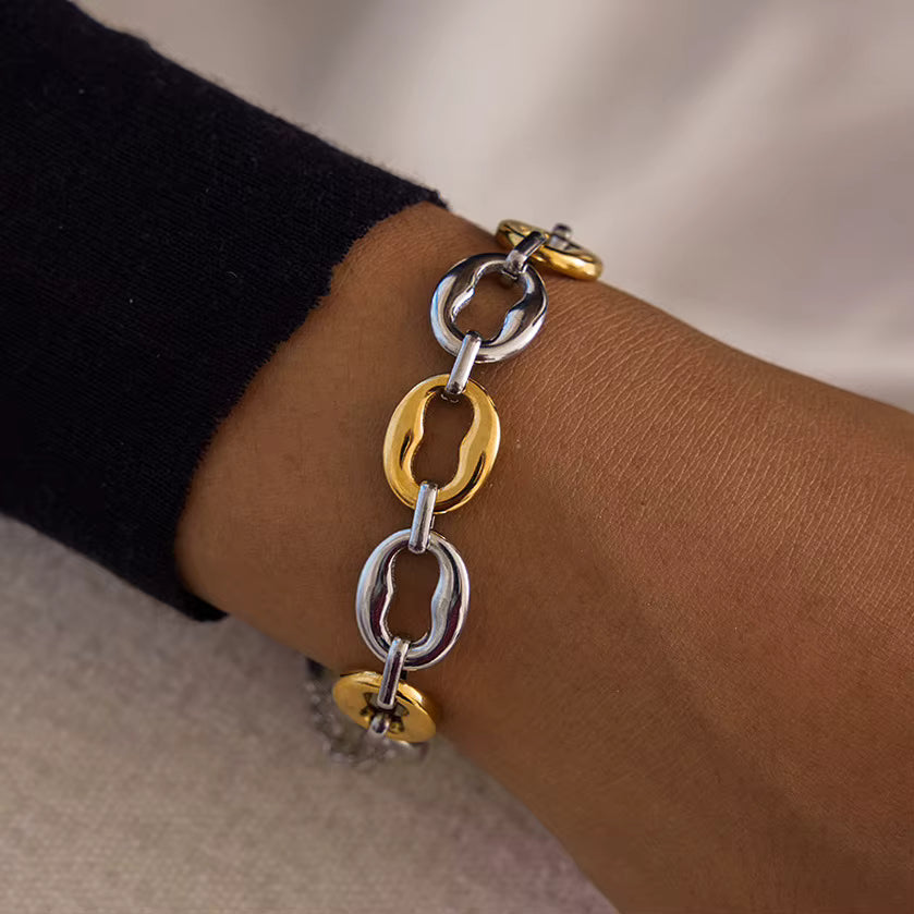 Bracelet with gold and silver links on a wrist against a neutral background