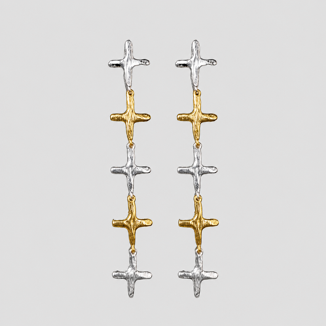 GRISÉ NYC 2-tone stainless steel cross dangle earrings featuring alternating 18k gold-plated and silver cross charms on a light gray background.
