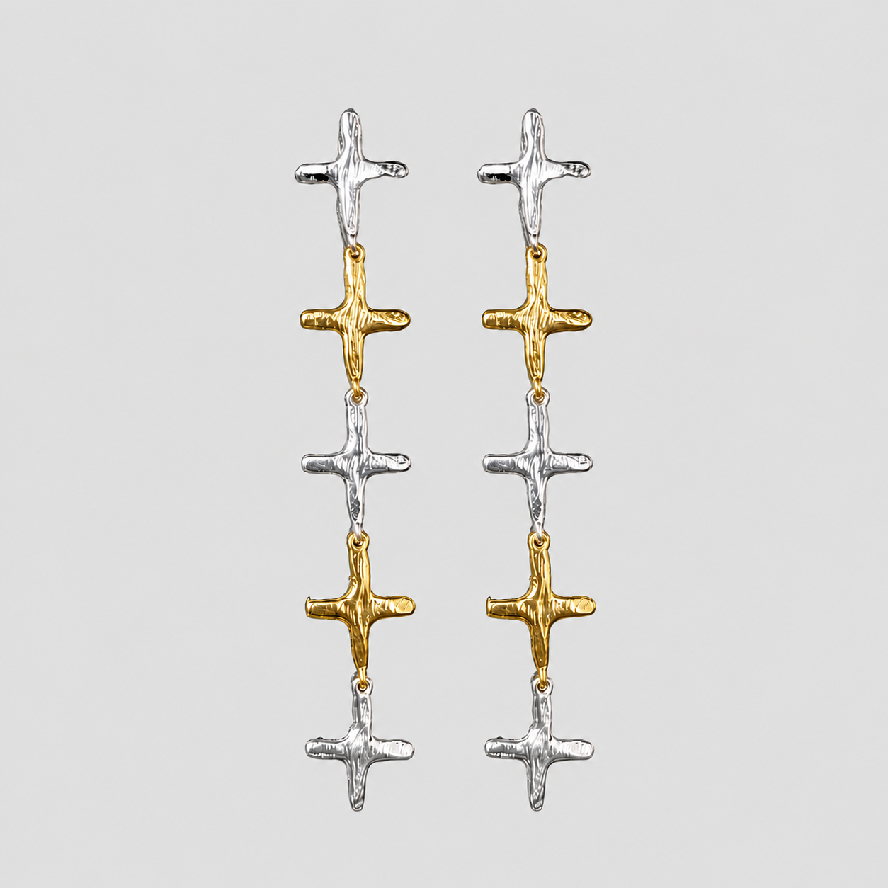 GRISÉ NYC 2-tone stainless steel cross dangle earrings featuring alternating 18k gold-plated and silver cross charms on a light gray background.