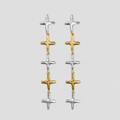 GRISÉ NYC 2-tone stainless steel cross dangle earrings featuring alternating 18k gold-plated and silver cross charms on a light gray background.