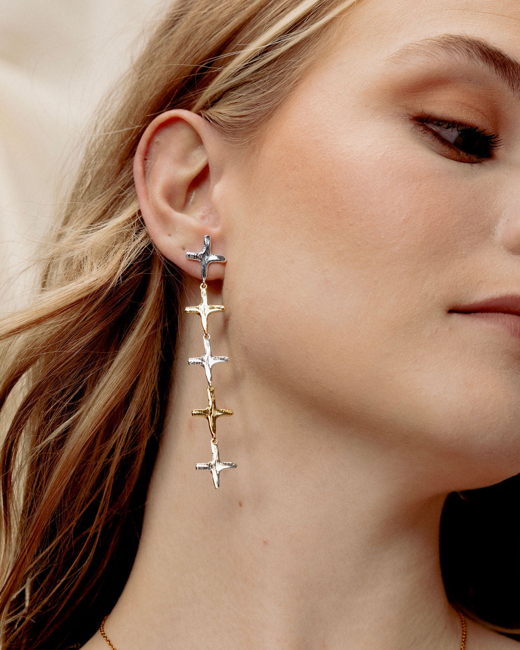 Model wearing 2-tone stainless steel cross dangle earrings with alternating 18k gold-plated and silver cross charms.