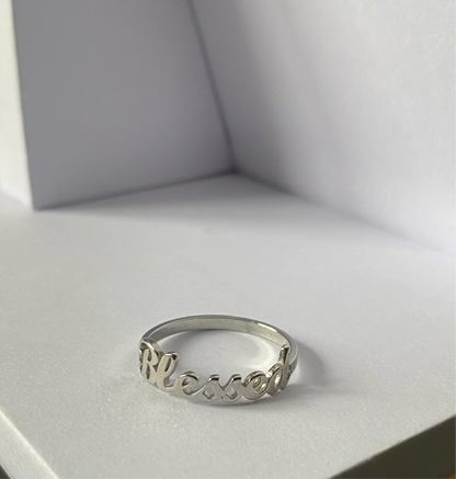 Blessed Ring in polished stainless steel displayed on a minimalist white surface by GRISÉ NYC.