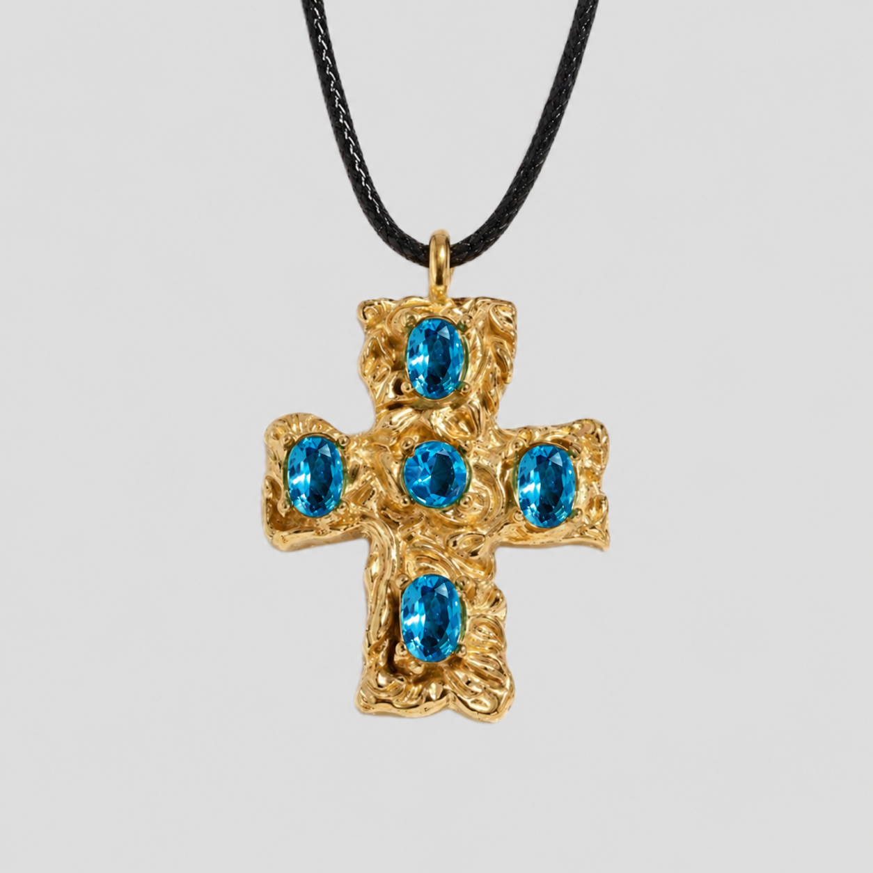 GRISÉ NYC Blue gemstone cross pendant necklace in gold with five oval blue stones on a black cord necklace against a light gray background.