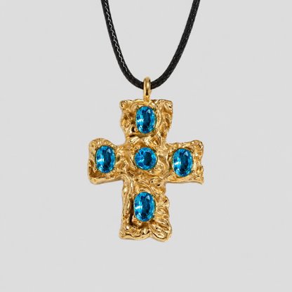 GRISÉ NYC Blue gemstone cross pendant necklace in gold with five oval blue stones on a black cord necklace against a light gray background.