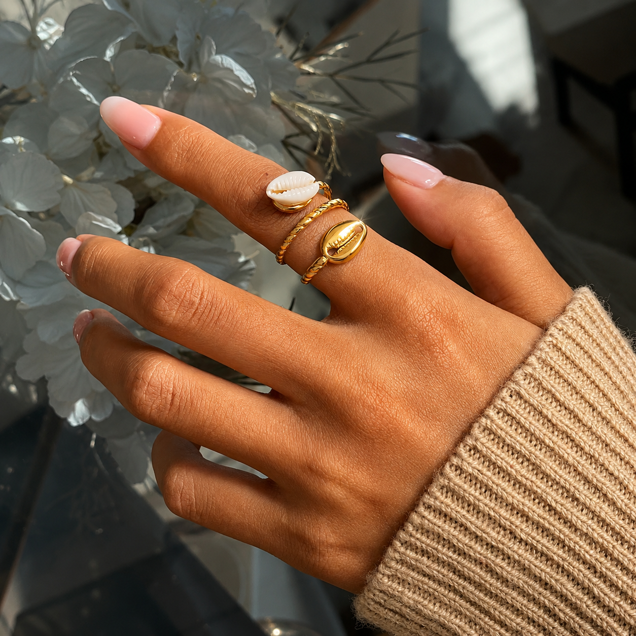 Model wearing the Cowrie Shell 18K Gold Ring featuring an adjustable twisted gold band with dual cowrie shell accents, styled with a cozy knit sweater by GRISÉ NYC.
