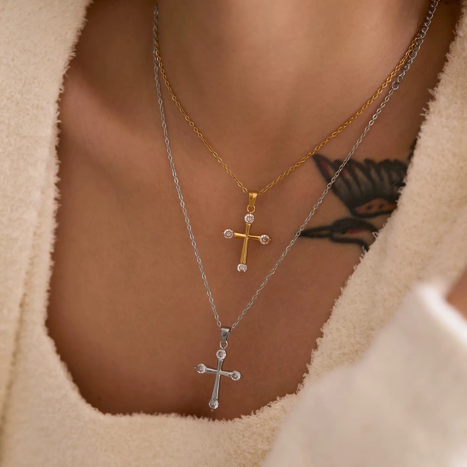 Model wearing layered Eterna cross pendant necklaces in 18K gold and stainless steel with cubic zirconia accents by GRISÉ NYC.