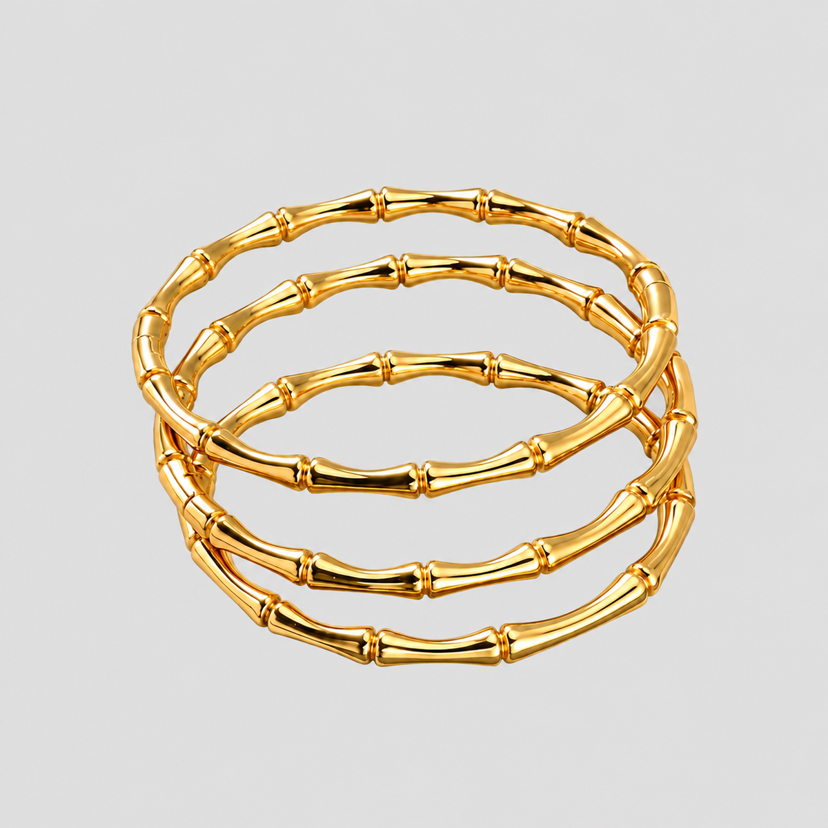 Three polished gold bamboo bangle bracelets stacked together, featuring sculptural segmented bamboo detailing on a light grey background by GRISÉ NYC.