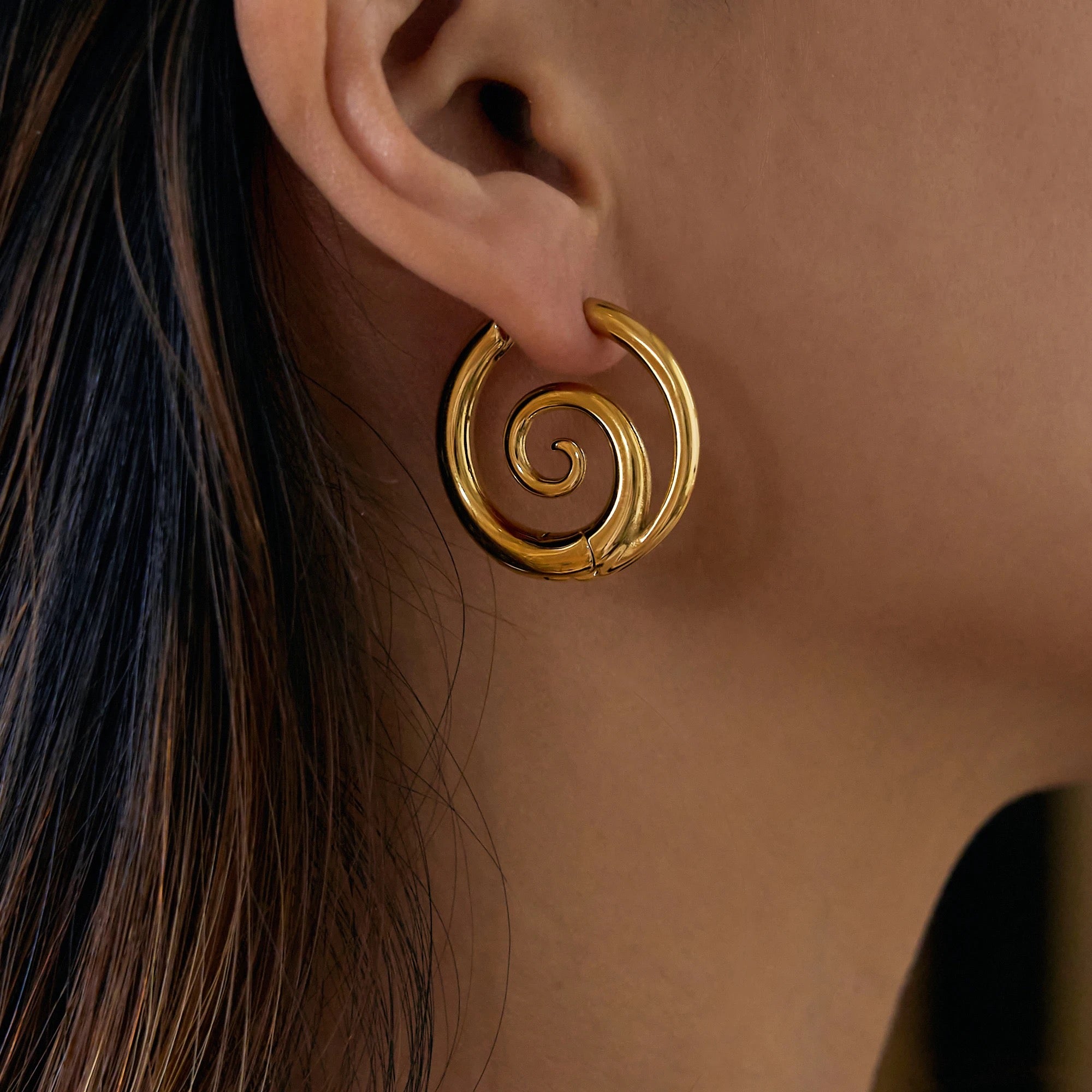 Model wearing GRISÉ NYC 18k gold spiral hoop earrings bold statement gold earrings on ear.