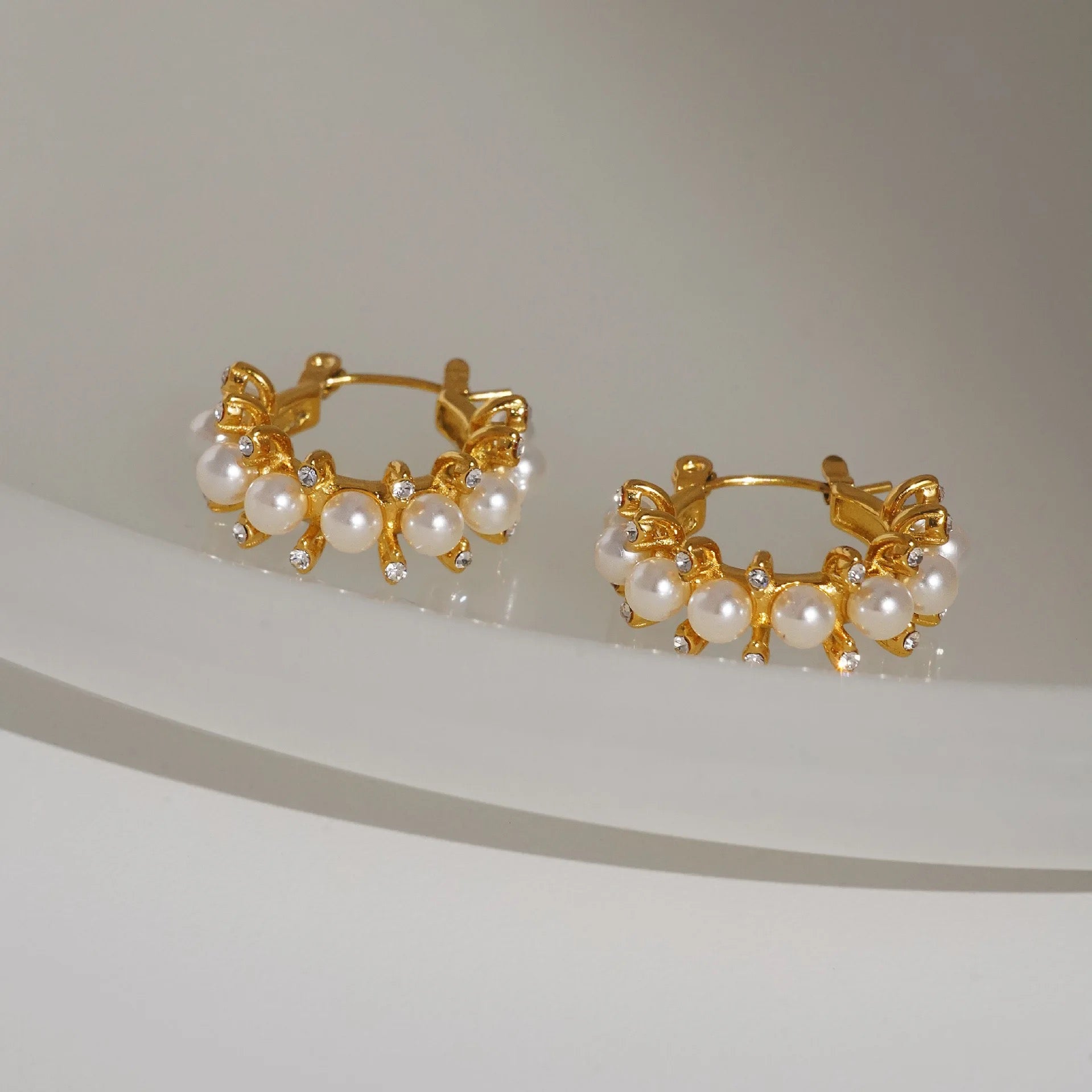 Flat lay of adorned pearl hoop earrings with simulated pearls and gold plated stainless steel by GRISÉ NYC.