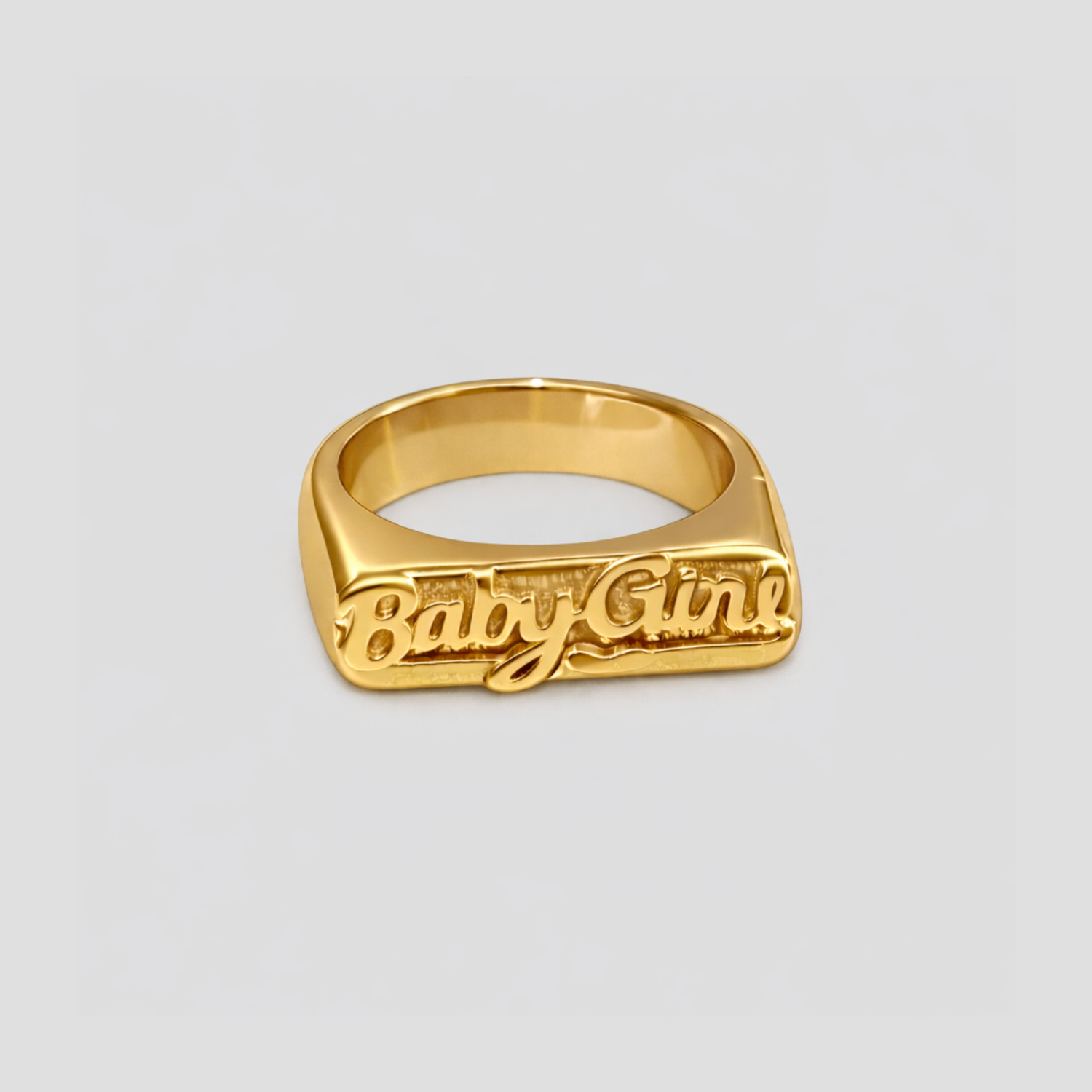 GRISÉ NYC Baby Girl signet ring in 18k gold plated stainless steel with raised cursive engraving on sleek rectangular face, front view on gray background.
