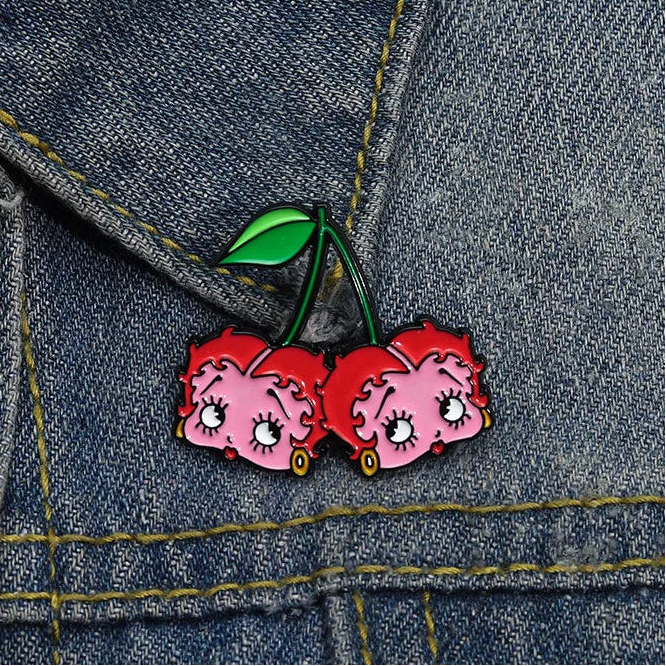 GRISÉ NYC Betty Boop Cherry Enamel Pin styled on denim jacket featuring pink and red cherry character design with green enamel stem detailing