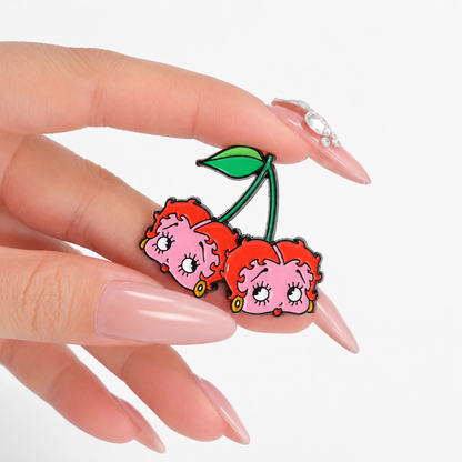 GRISÉ NYC Betty Boop Cherry Enamel Pin held in hand featuring pink and red cherry characters with glossy enamel detailing