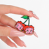 GRISÉ NYC Betty Boop Cherry Enamel Pin held in hand featuring pink and red cherry characters with glossy enamel detailing