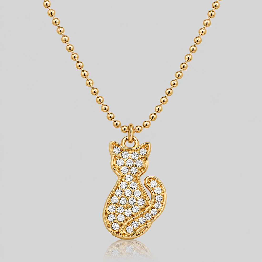 GRISÉ NYC Cat Charm Pendant Necklace in 18k gold plated stainless steel with crystal rhinestone detailing on a gold ball chain against a light grey background