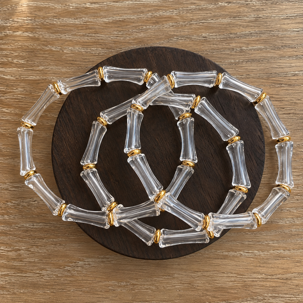 Clear transparent bamboo-inspired bangle bracelets featuring polished gold-tone accents, arranged in overlapping layers on a dark wooden display by GRISÉ NYC.