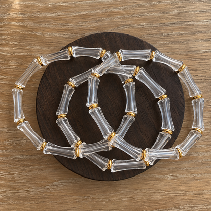 Clear transparent bamboo-inspired bangle bracelets featuring polished gold-tone accents, arranged in overlapping layers on a dark wooden display by GRISÉ NYC.