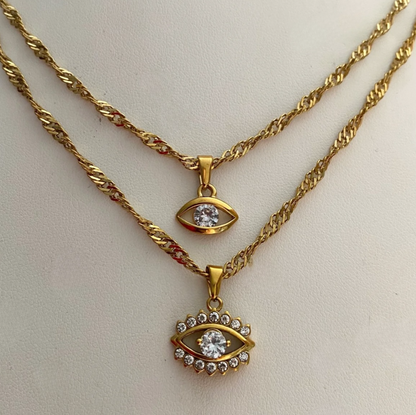 GRISÉ NYC layered gold evil eye pendant necklaces featuring twisted chains, sparkling cubic zirconia accents, and 18k gold-plated stainless steel construction.