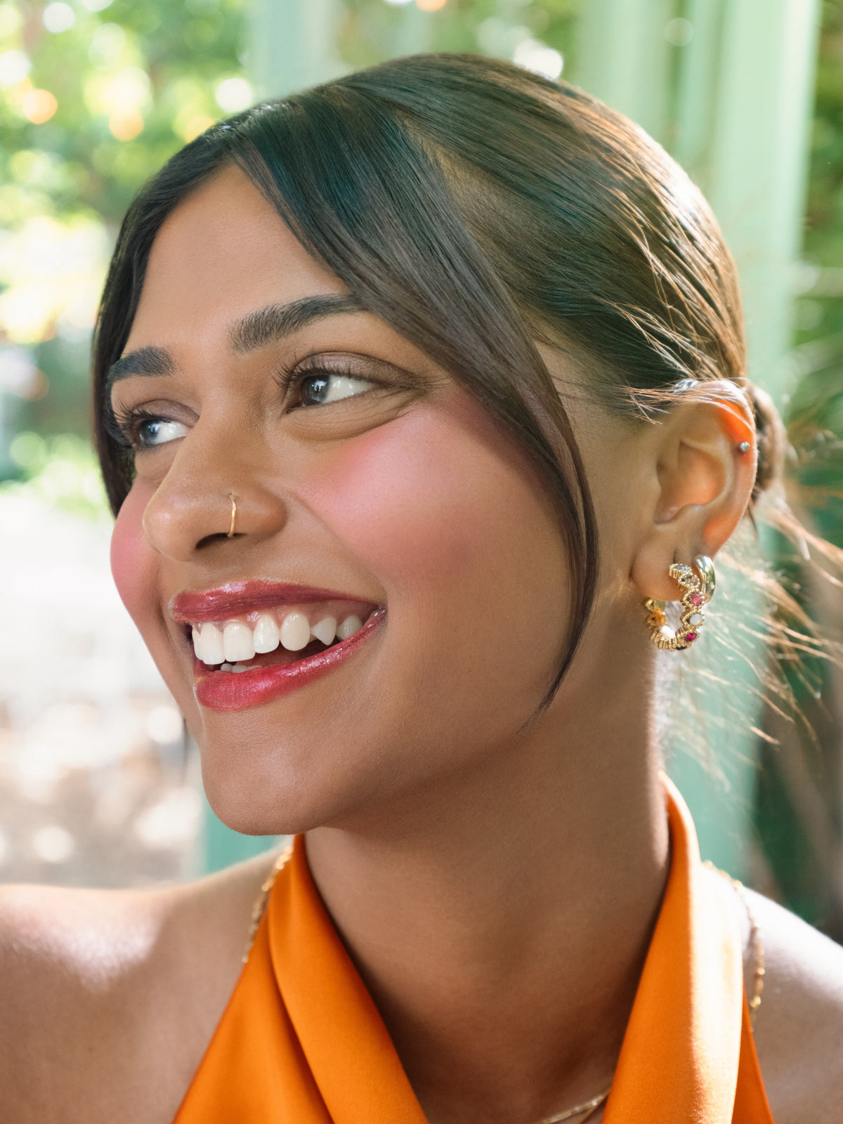 Model wearing GRISÉ NYC Gemma Multicolor Gold Hoop Earrings featuring colorful cubic zirconia stones, styled with an orange halter top for the Kulfi Beauty campaign.