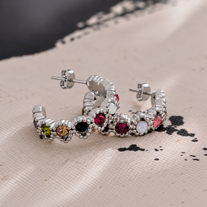 GRISÉ NYC Gemma Multicolor Silver Hoop Earrings featuring colorful cubic zirconia stones and butterfly backs, styled on textured beige fabric.