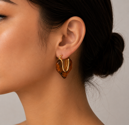 Close-up of model wearing GRISÉ NYC Gold Molten Heart Amber Resin Hoop Earrings in 18k gold-plated stainless steel with translucent amber resin heart design.