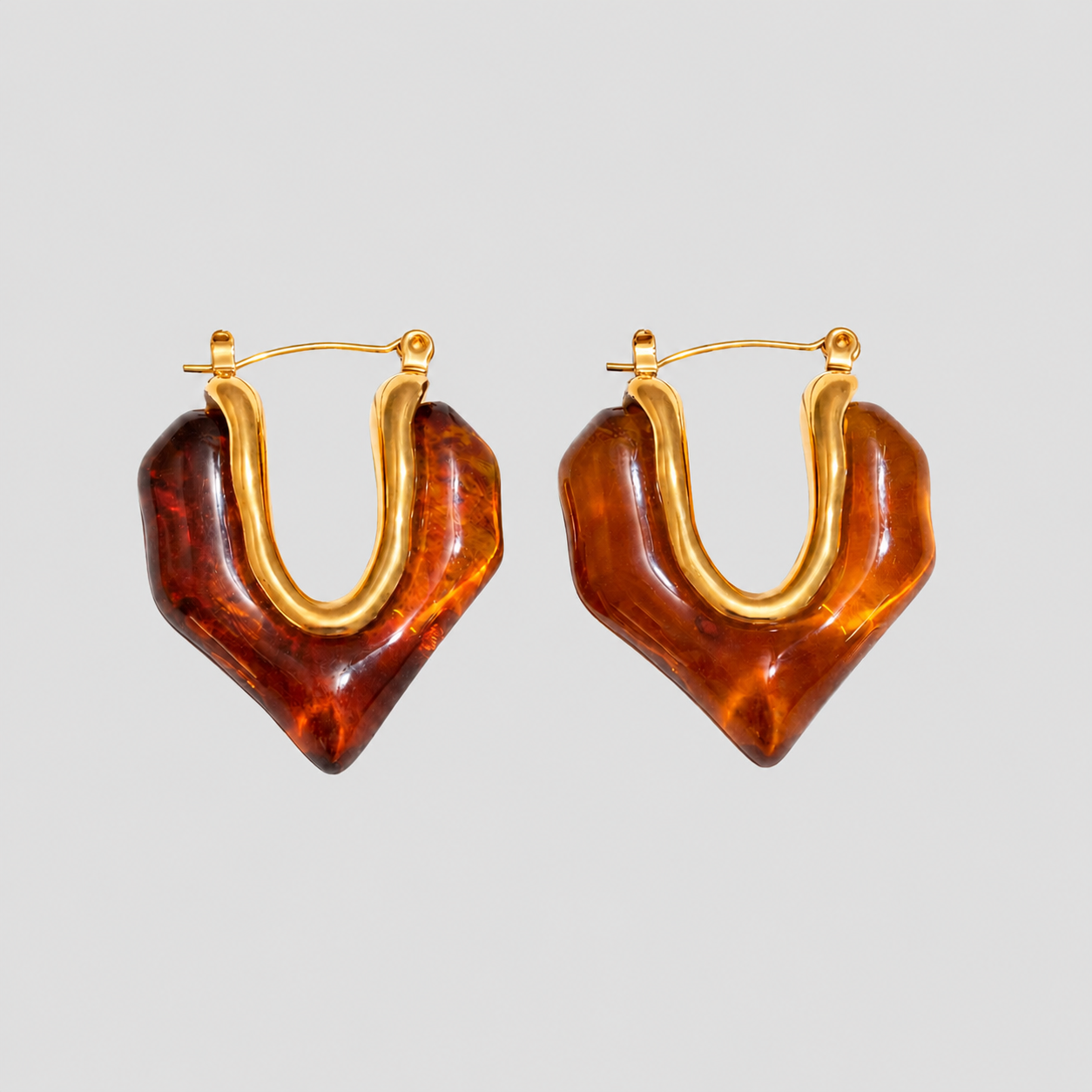 Gold Molten Heart Amber Resin Hoop Earrings in 18k gold-plated stainless steel with translucent amber resin heart design on a light gray background.