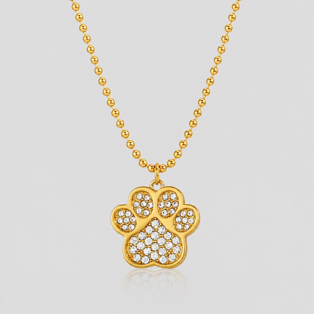 GRISÉ NYC Lucky Paw Crystal Necklace in 18k gold plated stainless steel with sparkling crystal rhinestone paw pendant on light gray background