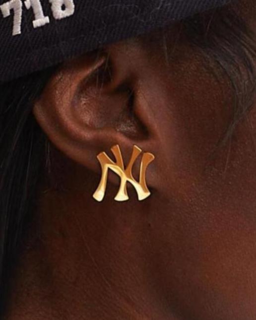 Close up of GRISÉ NYC New York Yankees NY logo stud earrings in gold worn on ear showing polished finish and everyday unisex styling.