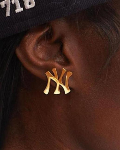 Close up of GRISÉ NYC New York Yankees NY logo stud earrings in gold worn on ear showing polished finish and everyday unisex styling.