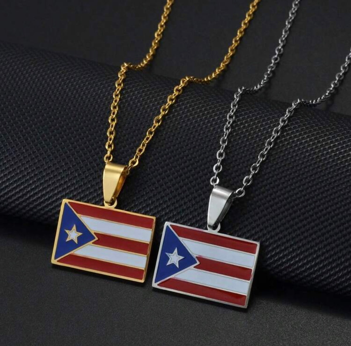 Gold and silver Puerto Rico flag pendant necklaces by GRISÉ NYC displayed on a black textured background.