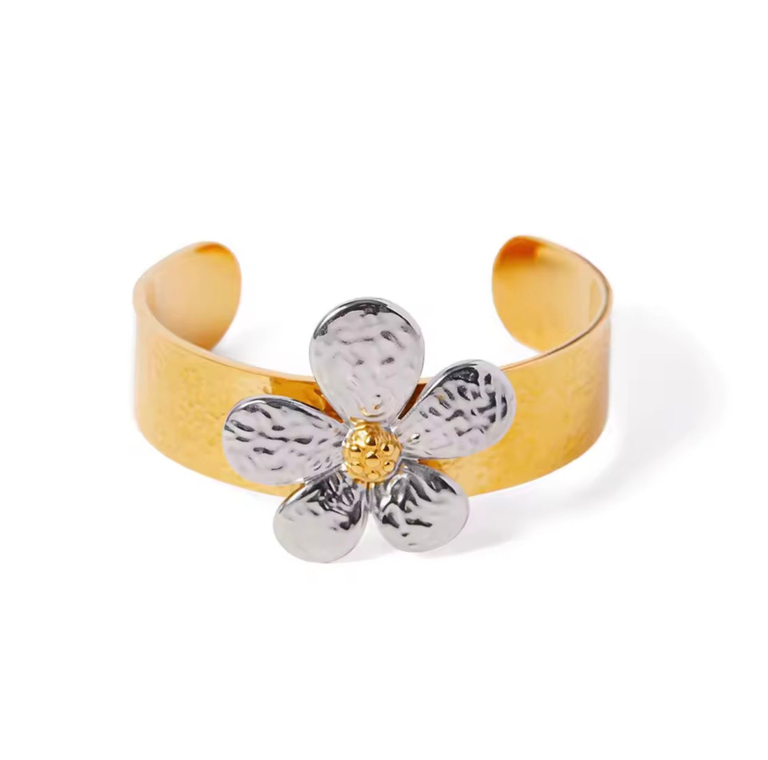 GRISÉ NYC two-tone floral adjustable cuff bracelet featuring a wide gold-tone band, textured silver flower petals, and a gold center on a light grey background.