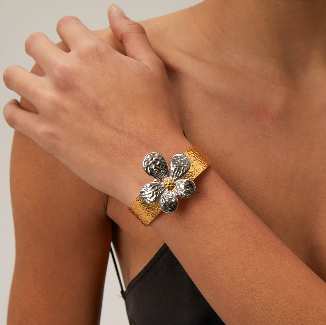 Model wearing the GRISÉ NYC two-tone floral adjustable cuff bracelet, featuring a gold-tone band and silver floral petals with a gold center.