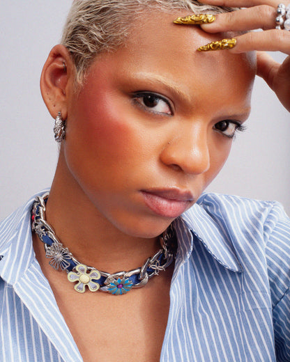 Model styling the GRISÉ NYC XL Cuban Link Charm Necklace featuring floral charms and blue woven chain details.