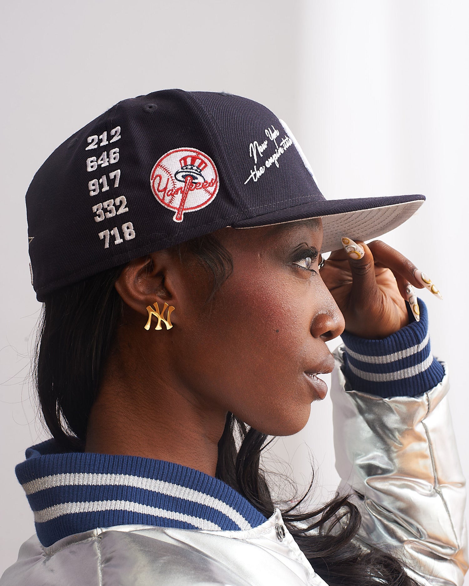 Side profile of female model wearing GRISÉ NYC gold New York NY logo stud earrings styled with black cap modern unisex streetwear look.