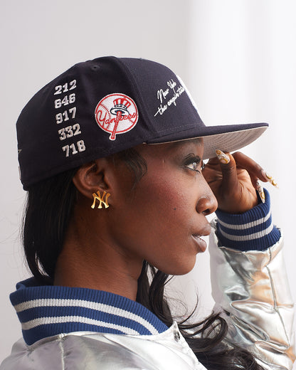 Side profile of female model wearing GRISÉ NYC gold New York NY logo stud earrings styled with black cap modern unisex streetwear look.