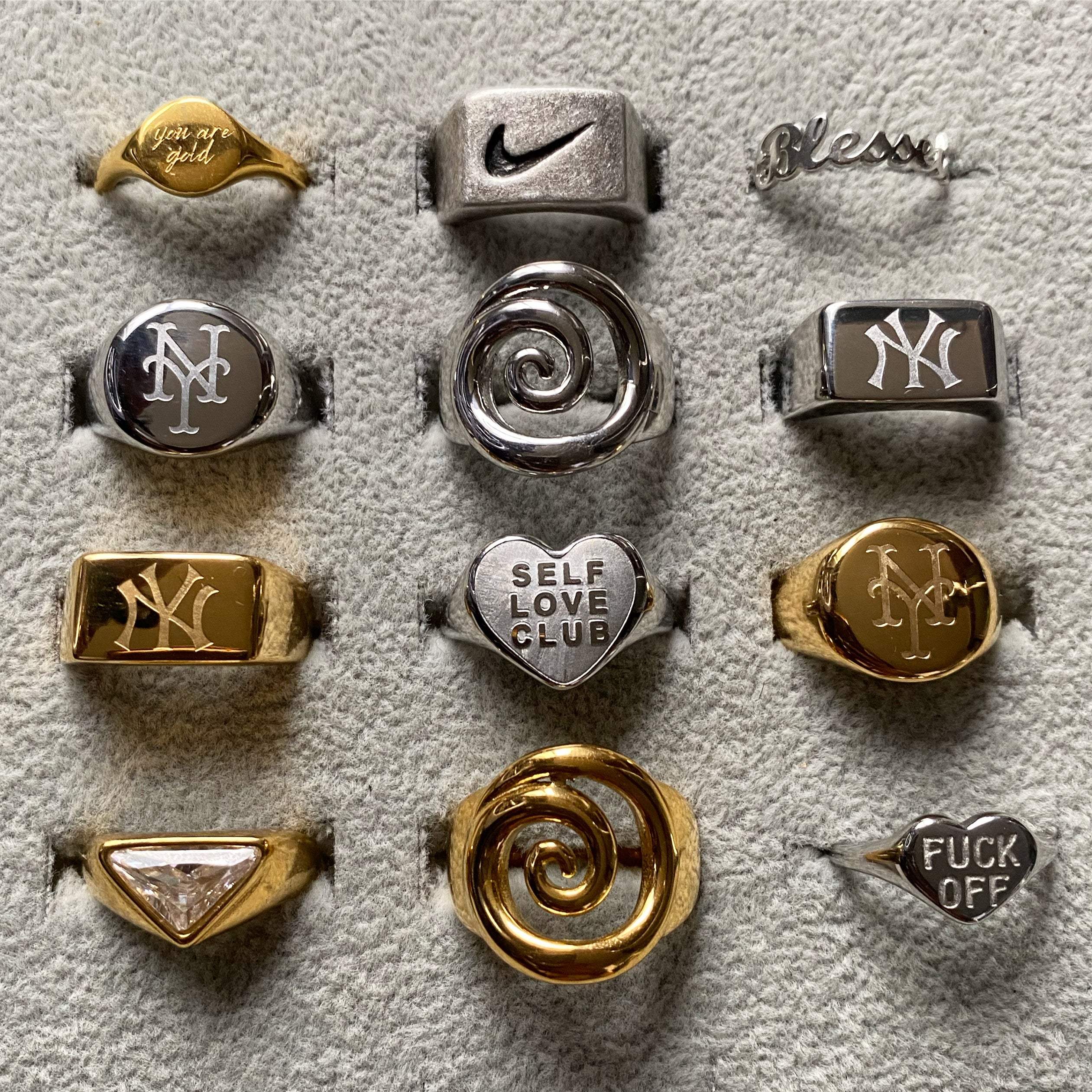 GRISÉ NYC stainless steel and 18k gold plated rings collection flat lay featuring New York signet rings spiral rings and statement unisex jewelry designs.