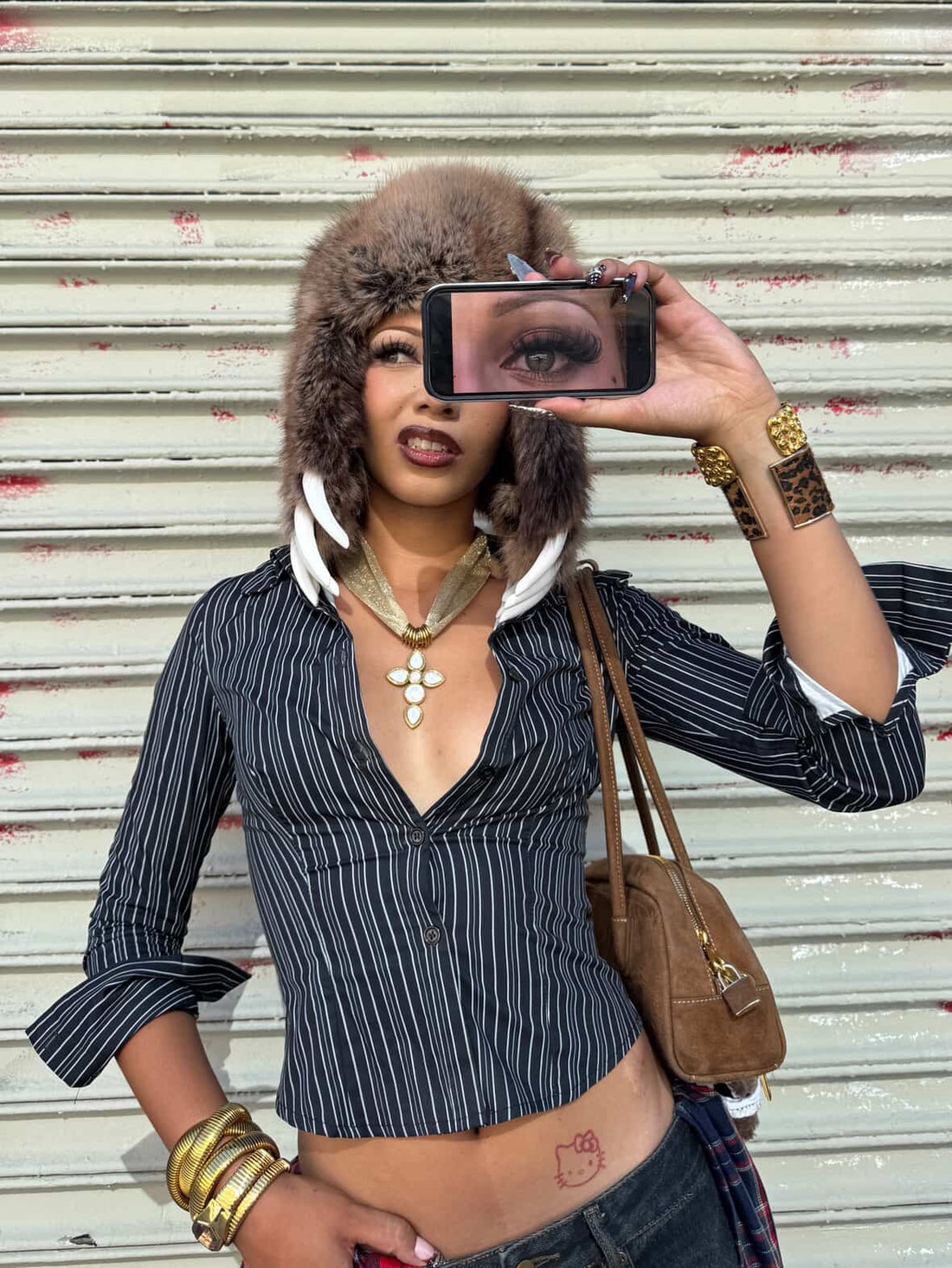 Model taking a selfie with a phone, wearing the gold plated cross pendant necklace with white quartz stones on mesh chain by GRISE NYC.
