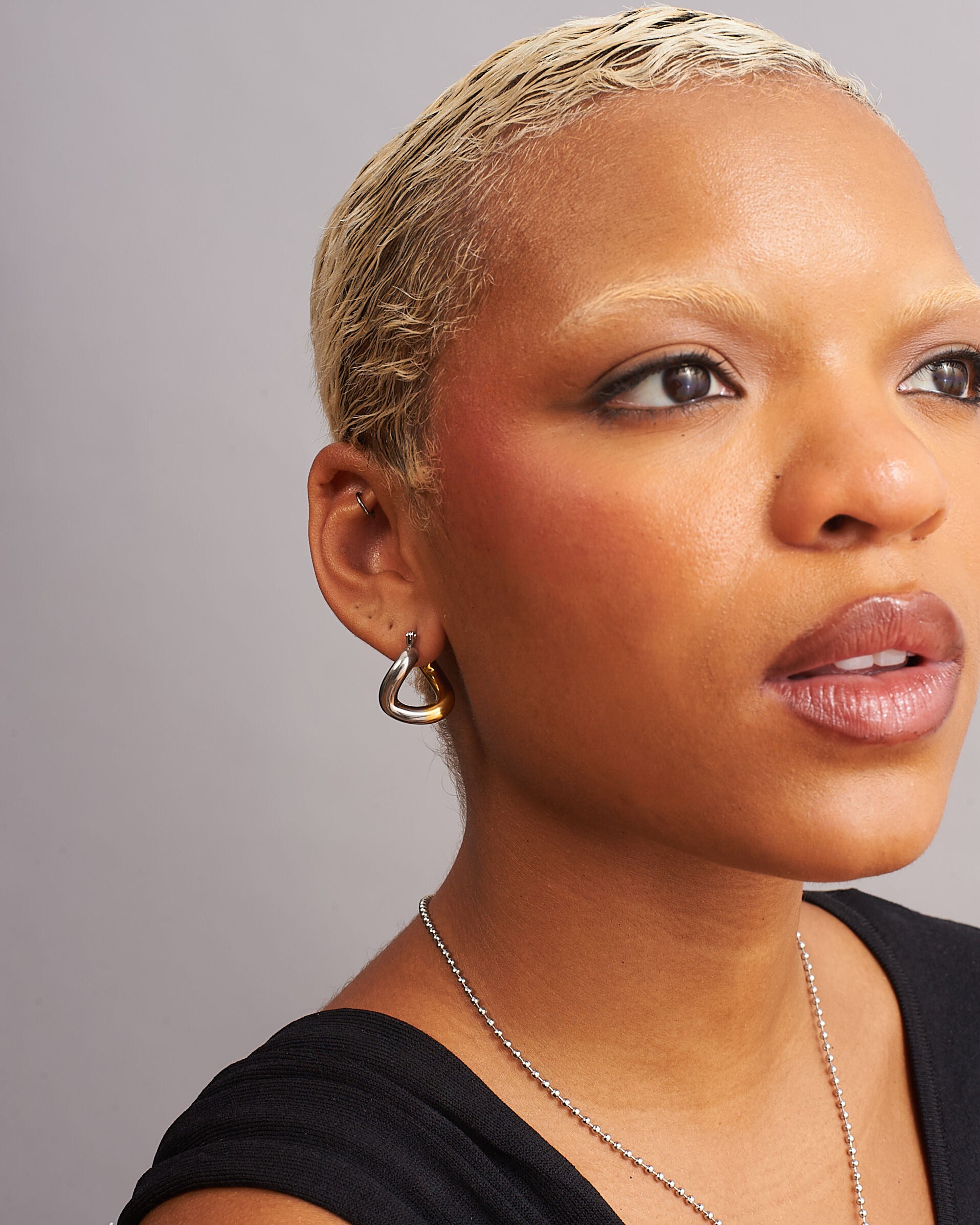 Model wearing modern two-tone gold and silver sculptural trapezoid twist hoop earrings by GRISÉ NYC.