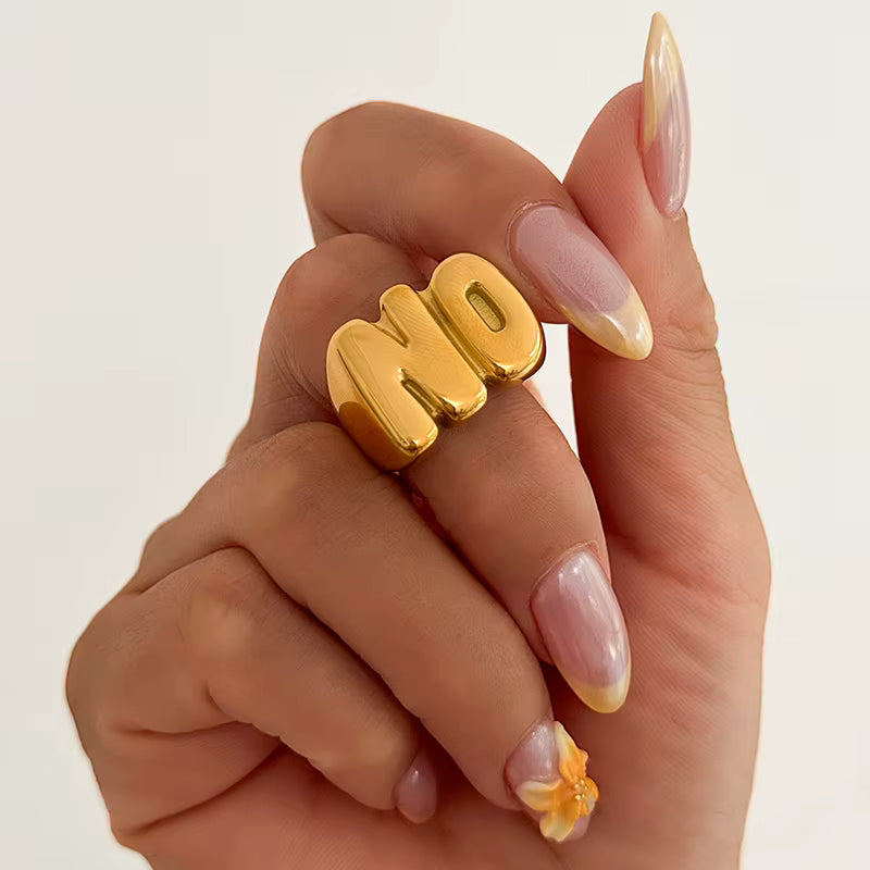 Model hand wearing the NO Letter 18k Gold Ring by GRISÉ NYC, styled with neutral nails and gold accessories for a playful statement look.