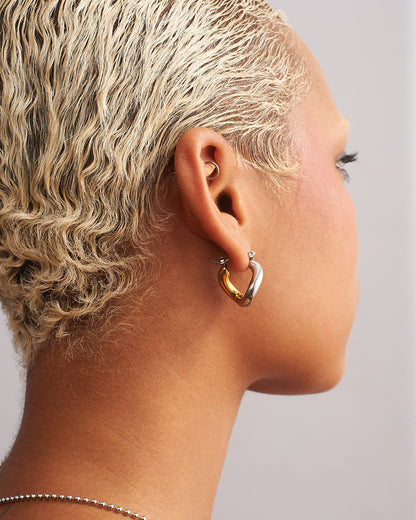 Model wearing two-tone trapezoid twist hoop earrings in polished 18K gold-plated stainless steel by GRISÉ NYC.